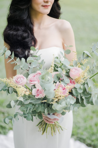 Hermosa novia vestida de novia sonrió alegremente y con un ramo de flores