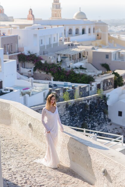 Hermosa novia con un vestido blanco posando en el contexto de la ciudad de Thira, Santorini.