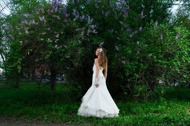 Hermosa novia con un vestido blanco sobre un fondo lila en primavera