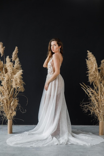 hermosa novia con un vestido blanco sobre un fondo negro cerca del paisaje seco de las flores