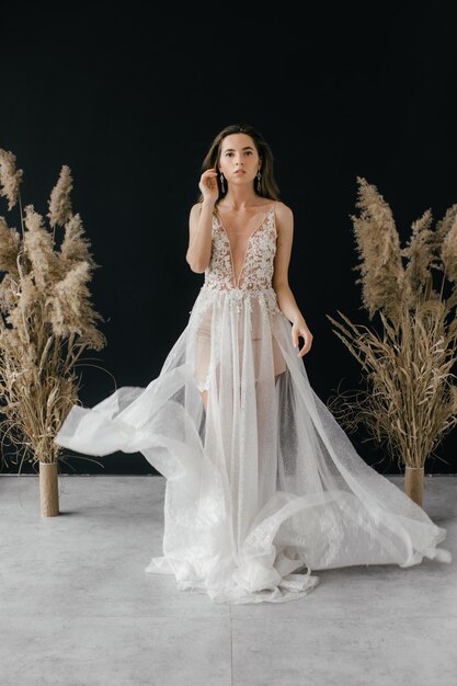 hermosa novia con un vestido blanco sobre un fondo negro cerca del paisaje seco de las flores