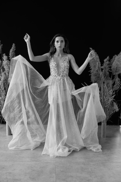 hermosa novia con un vestido blanco sobre un fondo negro cerca del paisaje seco de las flores