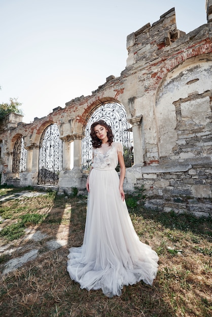 Hermosa novia en vestido de novia, que se fotografía en el día de la boda cerca del antiguo castillo.