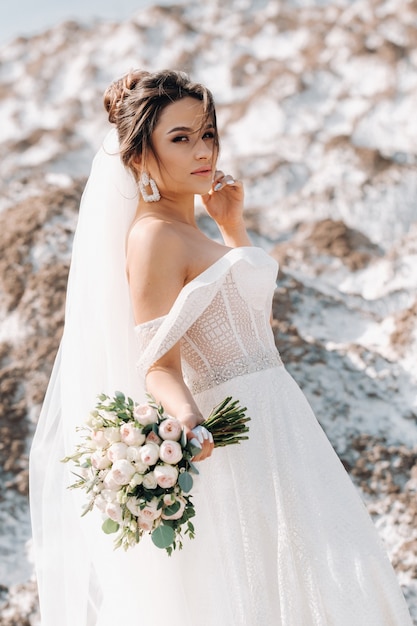 Hermosa novia en un vestido de novia con un ramo en la cima de las montañas de sal. Una deslumbrante joven novia de cabello rizado.