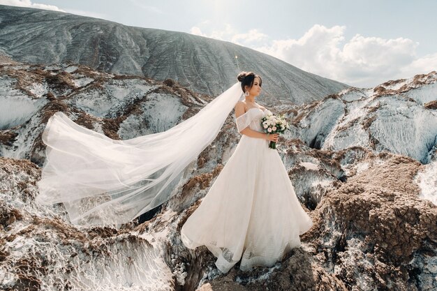 Hermosa novia en un vestido de novia con un ramo en la cima de las montañas de sal