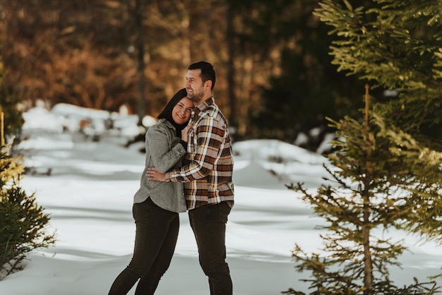 Hermosa pareja abrazándose entre pinos nevados mujer en ropa casual cogidos de la mano en el pecho del hombre Enfoque selectivo