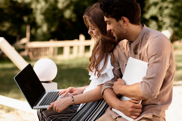 Una hermosa pareja adolescente hombre y mujeres que trabajan usan la computadora portátil para trabajar en el parque al aire libre de vacaciones