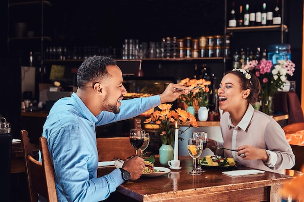 Hermosa pareja afroamericana enamorada pasando un buen rato juntos en su cita, una pareja atractiva disfrutando el uno del otro, un hombre guapo alimentando a su mujer en un restaurante.