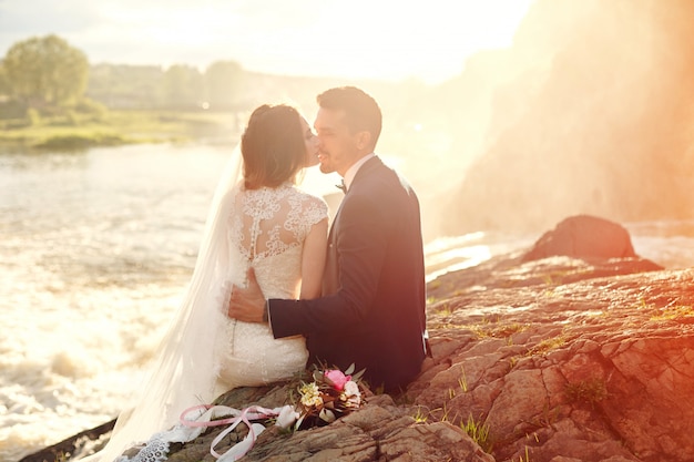 Hermosa pareja ama besarse mientras está sentado en las rocas cerca del río