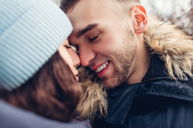 Hermosa pareja amorosa caminando y abrazándose en el bosque de invierno. Personas tocando narices. De cerca