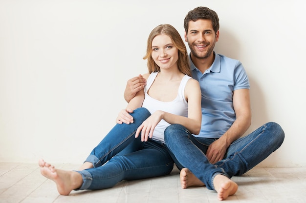 Hermosa pareja amorosa. Hermosa joven pareja amorosa sentada en el suelo en su apartamento y sonriendo a la cámara