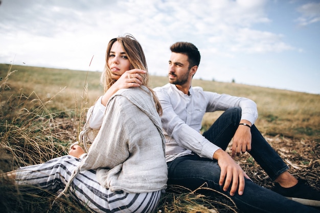 Hermosa pareja amorosa sentada sobre la hierba. El chico y la chica viajan hipster