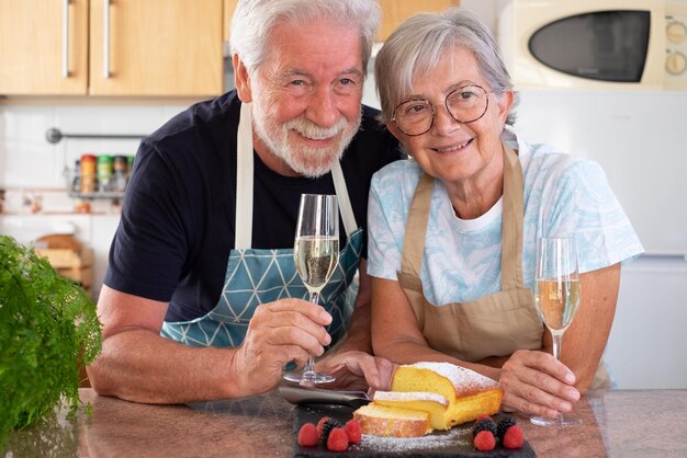 Hermosa pareja de ancianos en la cocina de casa sosteniendo una copa de vino lista para comer su plumcake casero