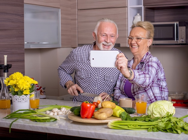 Foto hermosa pareja de ancianos cocinando en la cocina con los demás y viendo algo en el dispositivo