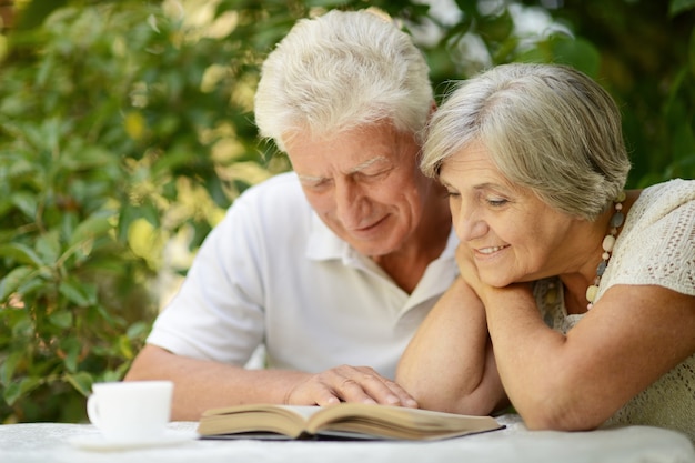 Hermosa pareja de ancianos descansando en el jardín en verano, leyendo un libro