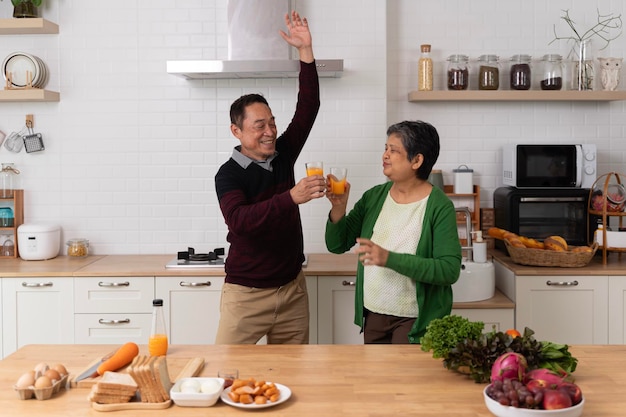 Una hermosa pareja de ancianos juguetona en delantales bailando y sonriendo mientras preparan una cena saludable en casa Una hermosa pareja de ancianos está bailando y sonriendo mientras cocinan juntos en la cocina