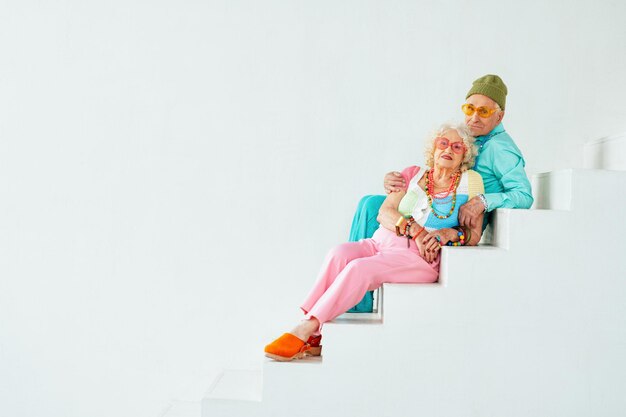 Hermosa pareja de ancianos con ropa de fiesta elegante actuando en el estudio sobre un fondo de color