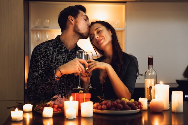 Hermosa pareja apasionada con una cena romántica a la luz de las velas en casa, bebiendo vino, brindando