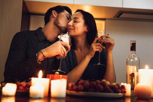 Hermosa pareja apasionada con una cena romántica a la luz de las velas en casa, bebiendo vino, brindando