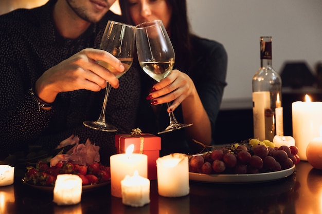 Hermosa pareja apasionada con una cena romántica a la luz de las velas en casa, bebiendo vino, brindando