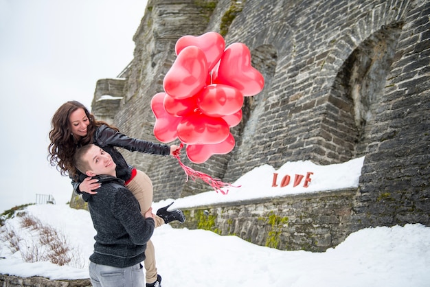 Hermosa pareja caminando en la ciudad de invierno con globos rojos. Historia de amor con un hombre y una mujer en la ciudad europea Old Tallinn