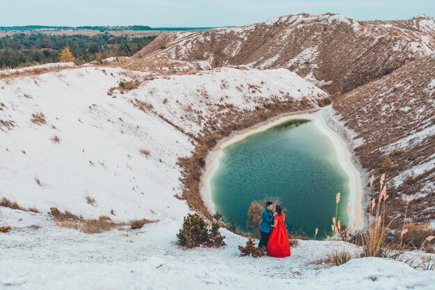 Hermosa pareja caminando en las montañas blancas de fosfato yeso de Ucrania la chica en un vestido rojo sobre un fondo de un lago verde