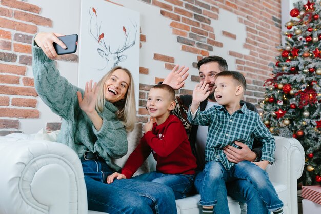 Hermosa pareja casada feliz con dos hijos usando un teléfono inteligente hablando con amigos o familiares felicita Feliz Navidad por la aplicación de videoconferencia. Tecnología moderna Año Nuevo 2022 felicidades.