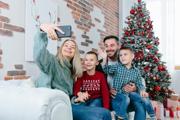 Hermosa pareja casada feliz con dos hijos usando un teléfono inteligente hablando con amigos o familiares felicita Feliz Navidad por la aplicación de videoconferencia. Tecnología moderna Año Nuevo 2022 felicidades.