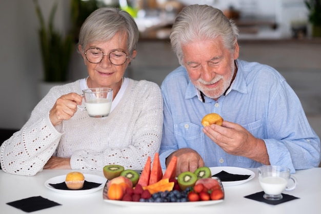 Foto hermosa pareja caucásica de ancianos jubilados desayunando en casa con leche de fruta fresca de temporada y concepto de alimentación saludable de cupcakes