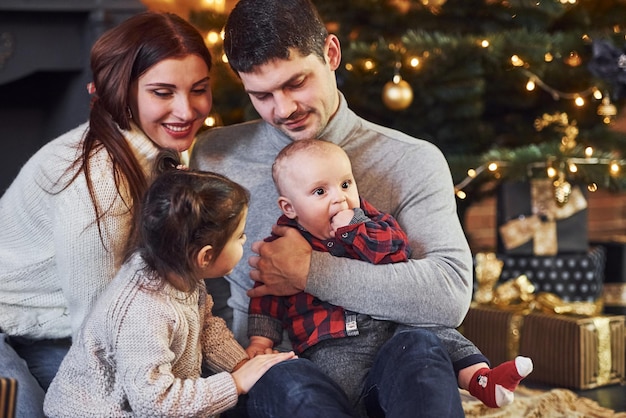 Hermosa pareja caucásica celebrando la navidad en el interior con su pequeño hijo e hija.