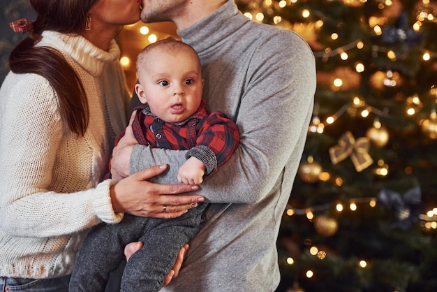 Hermosa pareja caucásica celebrando la navidad en el interior con su pequeño hijo.