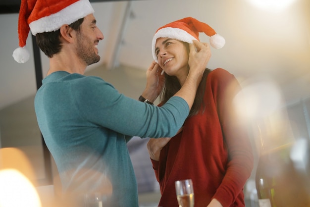 Hermosa pareja celebrando la Navidad en casa con champán y gorros de Papá Noel