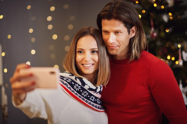 Hermosa pareja celebrando la Navidad en casa y tomando selfie