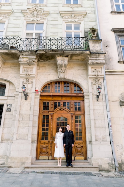 Hermosa pareja china posando junto a la antigua puerta marrón del antiguo edificio histórico en la antigua ciudad europea