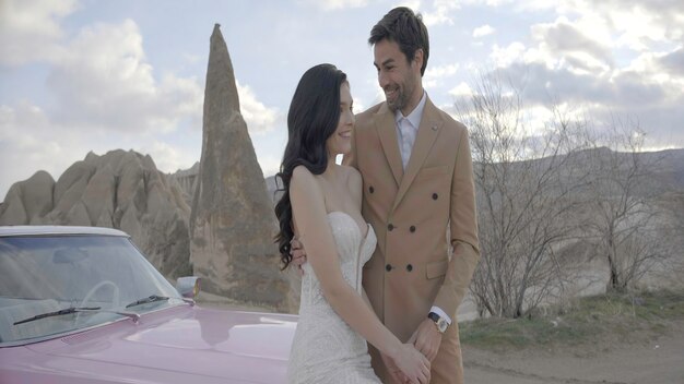 Hermosa pareja con coche en el fondo de las montañas acción elegantes trajes de los recién casados de vacaciones