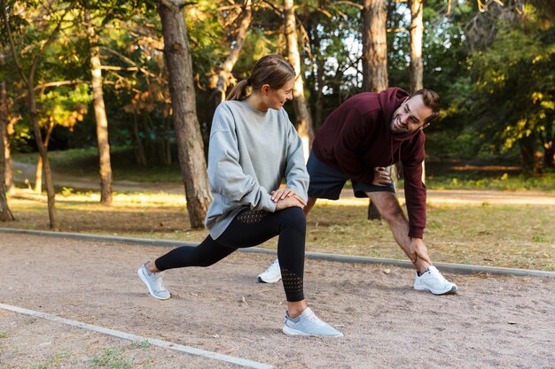 Hermosa pareja deportiva en ropa deportiva haciendo ejercicios mientras hace ejercicio en el parque verde durante el día soleado de verano