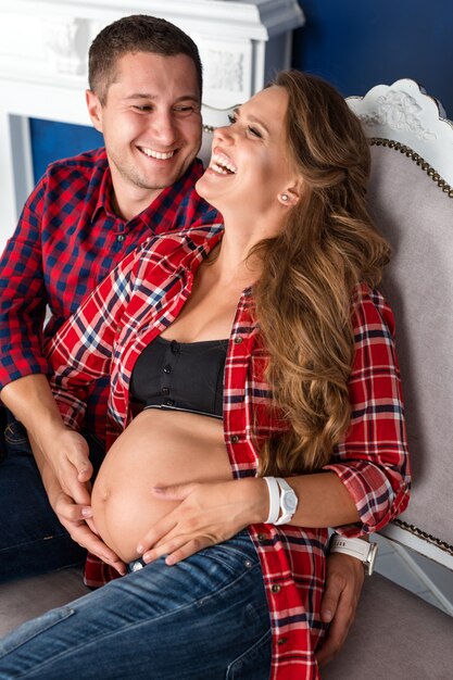 Hermosa pareja embarazada relajante en el sofá en casa juntos. Familia feliz, hombre y mujer esperando un hijo.