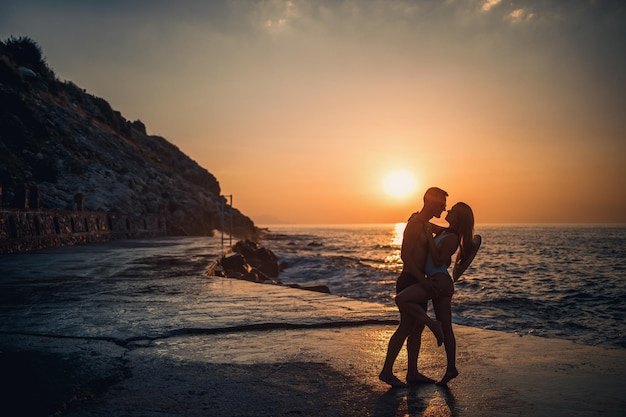Hermosa pareja enamorada en el fondo de la puesta de sol junto al mar Mujer joven y hombre abrazándose junto al mar al atardecer