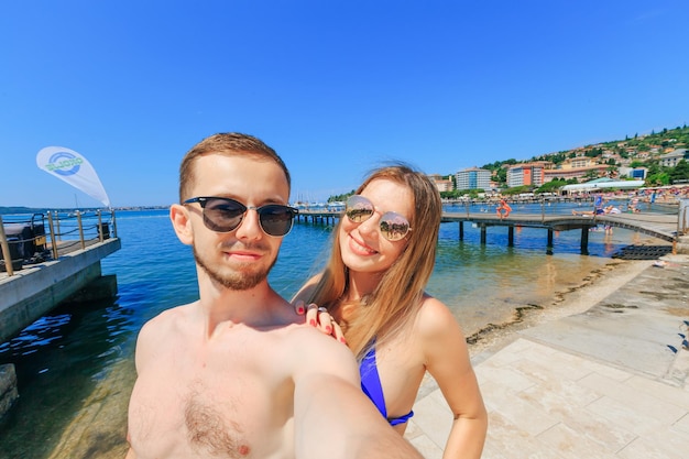 Foto hermosa pareja enamorada haciendo una selfie en la playa con vistas al mar y a la ciudad