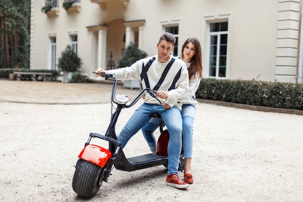 Hermosa pareja enamorada de la ropa de moda elegante montando una bicicleta electrónica cerca del hotel