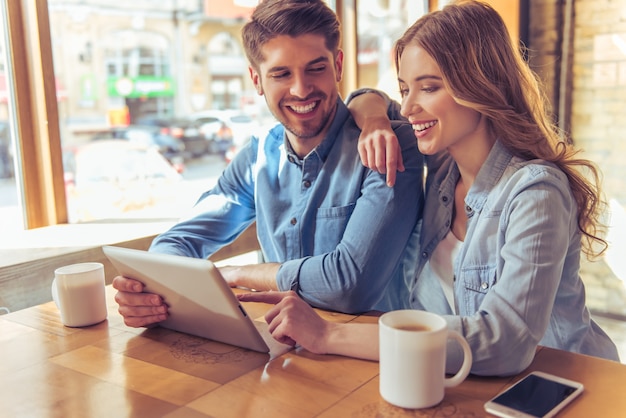 Hermosa pareja está usando una tableta, hablando y sonriendo.