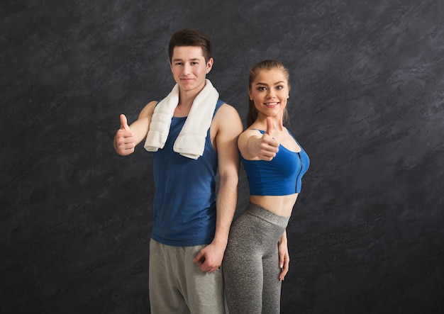 Hermosa pareja de fitness posando y mostrando los pulgares para arriba en el gimnasio. Retrato de mujer y hombre deportivo seguro con cuerpos perfectos, estilo de vida saludable y concepto de cuidado corporal, espacio de copia