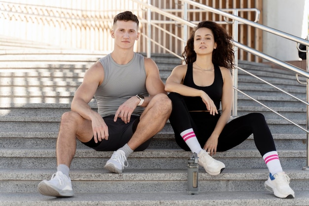 Hermosa pareja de fitness con ropa deportiva elegante sentada en las escaleras y posando en la calle de la ciudad