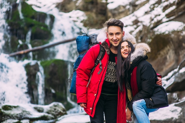 Hermosa pareja hipster sonriente de pie sobre una roca, montañas, cascada, sonrisa benévola dos chicos en la expedición aventura de montaña, par de moda de la diversión al aire libre