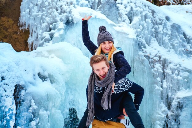 Hermosa pareja hipster sonriente de pie sobre una roca, montañas, cascada, sonrisa benevolente dos chicos en expedición de aventura en la montaña, par de moda de diversión al aire libre