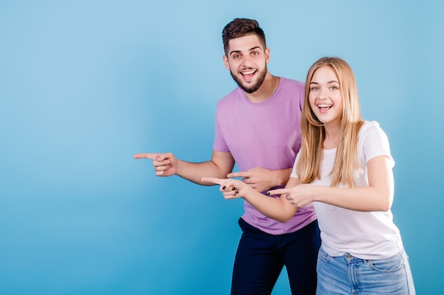 Hermosa pareja hombre y mujer señalando con el dedo en el espacio de copia en azul