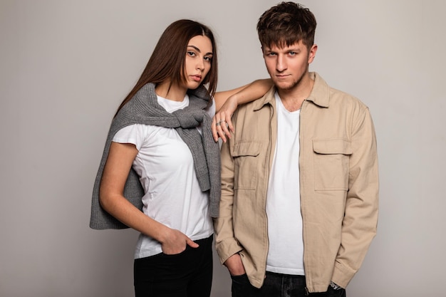 Foto hermosa pareja joven y elegante con ropa informal de moda con camisetas blancas, suéter de punto y chaqueta marrón en el estudio. mujer bonita y hombre guapo en ropa de moda