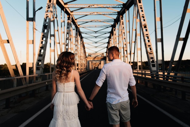 Una hermosa pareja joven enamorada de un hombre y una mujer abrazan un beso en un gran puente de metal al atardecer