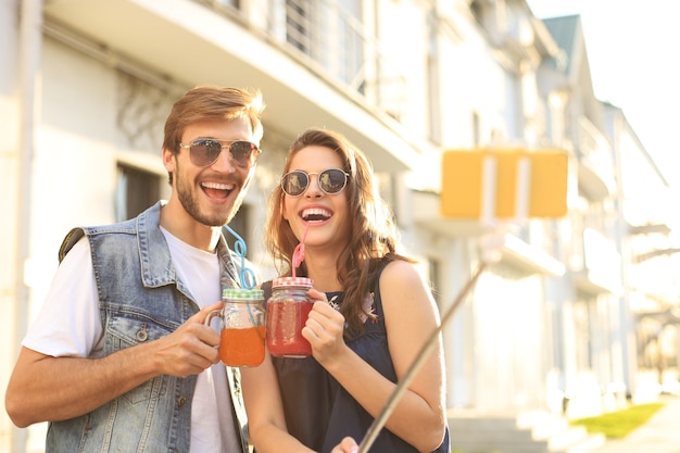 Hermosa pareja joven encantadora caminando por las calles de la ciudad, abrazándose mientras toma un selfie.