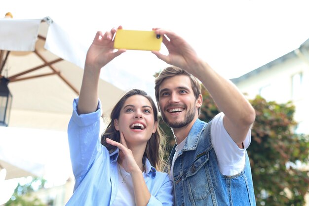 Hermosa pareja joven encantadora caminando por las calles de la ciudad, tomando un selfie.